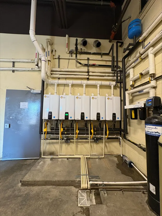 A row of tankless water heaters with new piping on a commercial wall